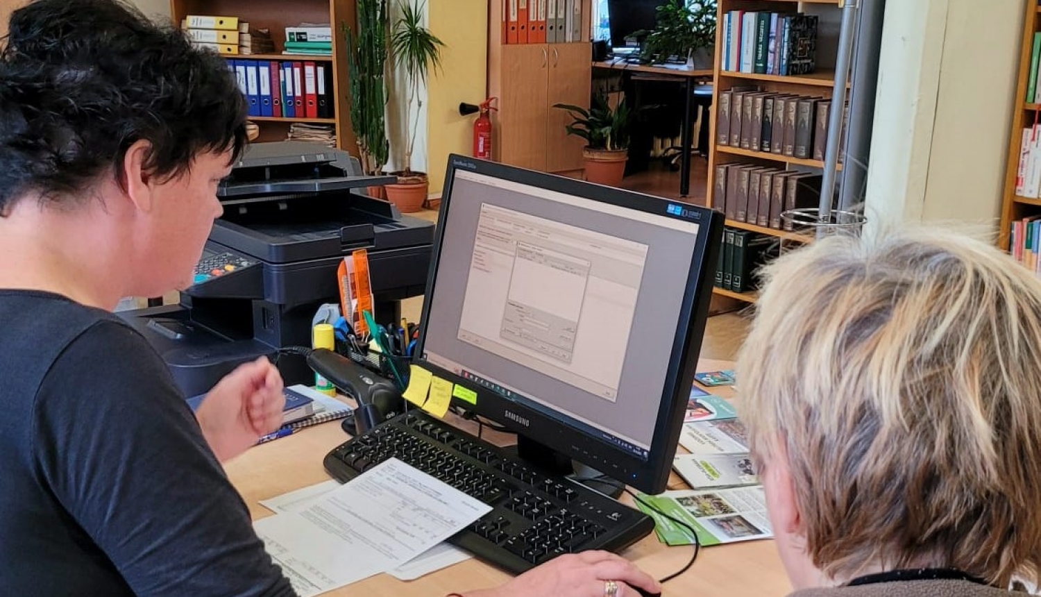 Ērgļu bibliotēkas bibliotekāre, KAC darbiniece Inga Stiebriņa palīdz apmeklētājai sagatavot atbalsta pieteikuma veidlapu